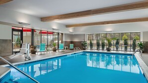 An indoor swimming pool with clear blue water, surrounded by lounge chairs and potted plants.