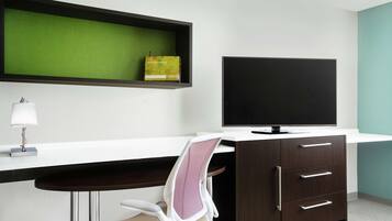 A modern office space with a desk, chair, TV, and a shelf with a book.