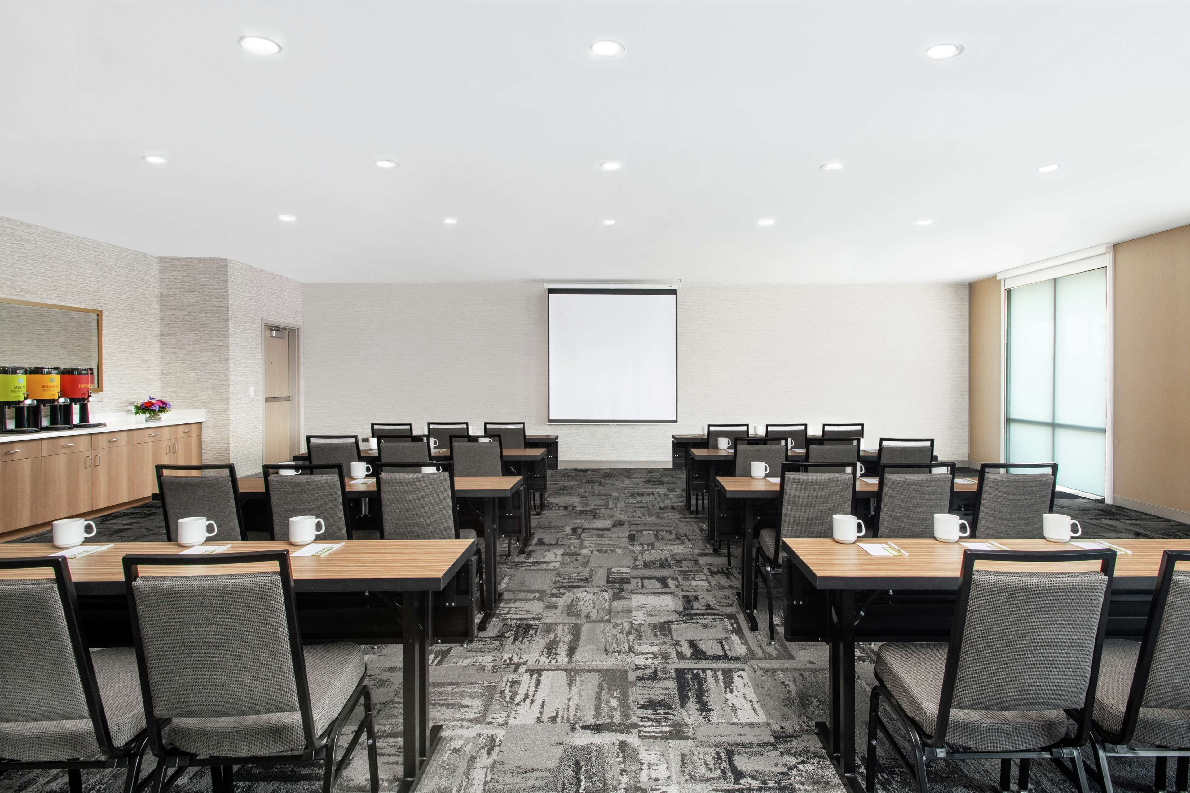 Una sala de conferències amb diverses taules i cadires, una pantalla de projector i un racó per fer cafè.