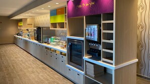 A modern kitchen area with a self-serve beverage station, a microwave, and various storage cabinets.