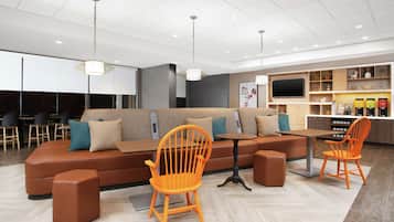 A modern lounge area with a brown sofa, orange chairs, a small table, and a TV.