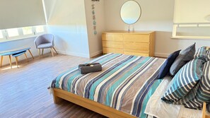 A bedroom with a wooden bed, striped bedding, a small desk, a chair, a dresser, and a mirror.