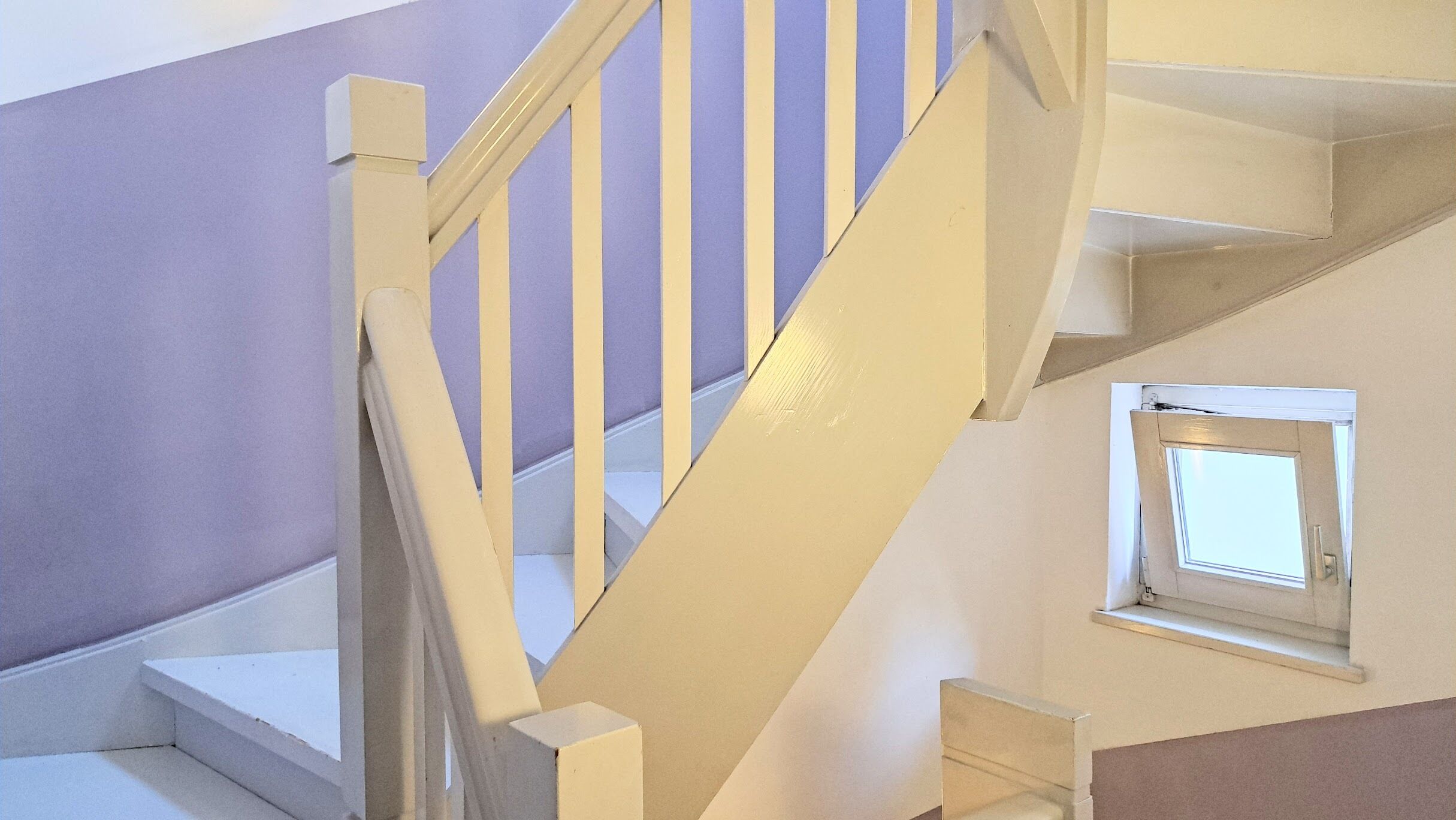 Un escalier avec des rampes blanches et une petite fenêtre sur le palier.