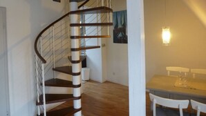 Una escalera de caracol con escalones de madera y barandillas de metal, que conduce a un comedor con una mesa y sillas.