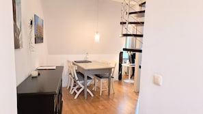 A dining area with a table and chairs, a small table with a lamp, and a painting on the wall. - Likedeeler at the city harbor, duplex apartment in the old town (Lübecker Altstadt)