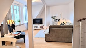 A modern living room with a TV, sofa, and a small table with books. - Likedeeler at the city harbor, duplex apartment in the old town (Lübecker Altstadt)