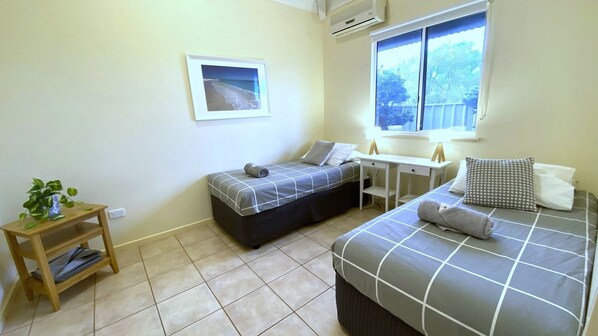 A small, clean room with two beds, a desk, a window, and a framed picture on the wall. - Osprey Holiday Village Unit 110 - Villa with a Pool in the Complex (EXMOUTH)