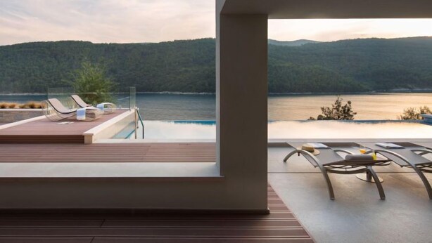 A modern outdoor lounge area with a pool, lounge chairs, and a view of a lake and forested hills. - Vlastelini II by Interhome (Labin)