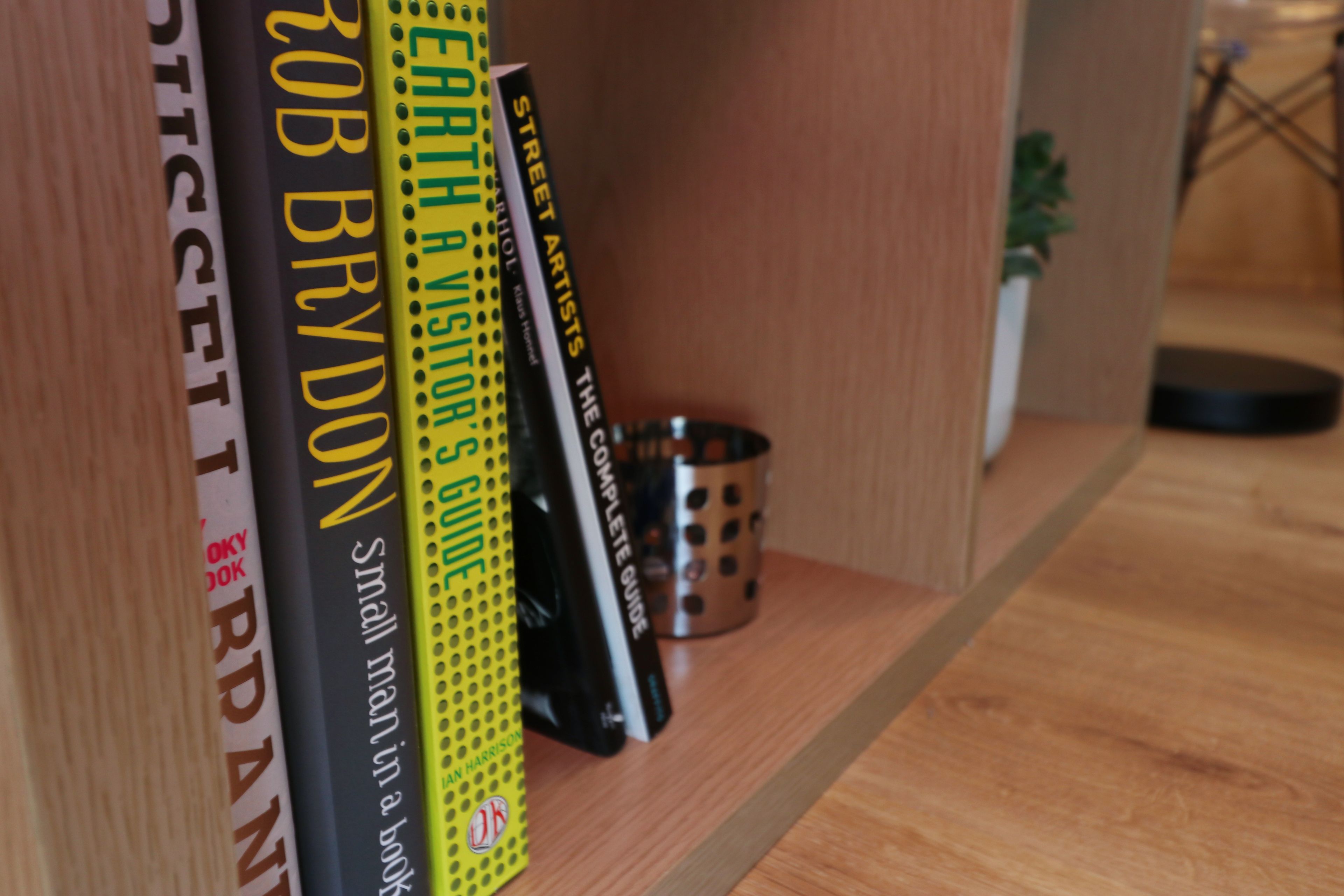 Une bibliothèque remplie de livres, un récipient en métal et une plante en pot.