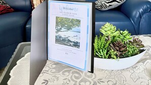 A blue sofa with a framed welcome sign, a small potted plant, and a framed picture of a beach on the wall. - New apartment in Pereybere (100 mt from the beach) (Pereybere)