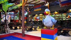 A bar area with a large bird sculpture, tables, chairs, and flags. - New apartment in Pereybere (100 mt from the beach) (Pereybere)
