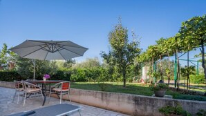 An outdoor patio with a table and chairs, a large umbrella, and potted plants. - Adriana by Interhome (Pula)