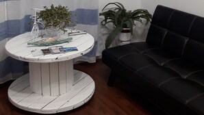 A living room with a striped curtain, a round white table with magazines, a black sofa, and a wall-mounted decorative item. - VILLASIMIUS CENTRO HOLIDAY HOUSE (Villasimius)