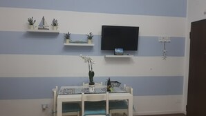A dining area with a table and chairs, a television mounted on the wall, and decorative items on shelves. - VILLASIMIUS CENTRO HOLIDAY HOUSE (Villasimius)