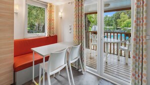 Un balcone con un tavolo e sedie bianche, una panca rossa e vista su una piscina e alberi.