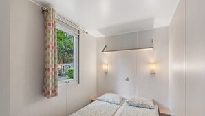 Una camera piccola con un letto singolo, una finestra, due luci a parete e una tenda.