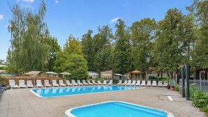 Una piscina rettangolare con lettini e ombrelloni bianchi, circondata da alberi e una recinzione.