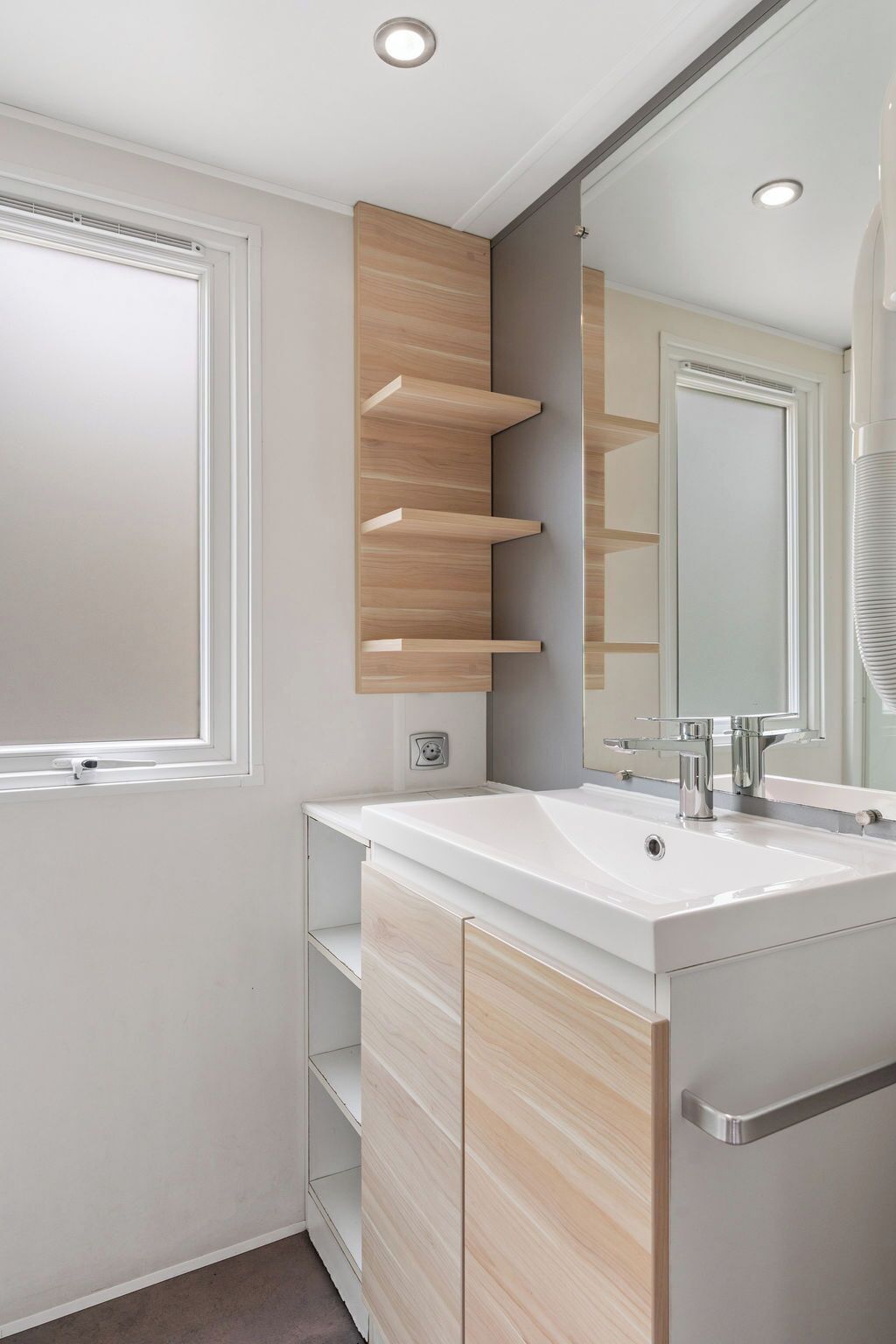 Un bagno moderno con un mobile lavabo bianco, uno specchio e scaffali a muro.