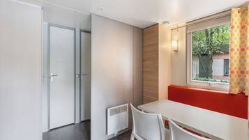 A modern room with a white table, two chairs, a bench, and a window with a view of greenery outside.