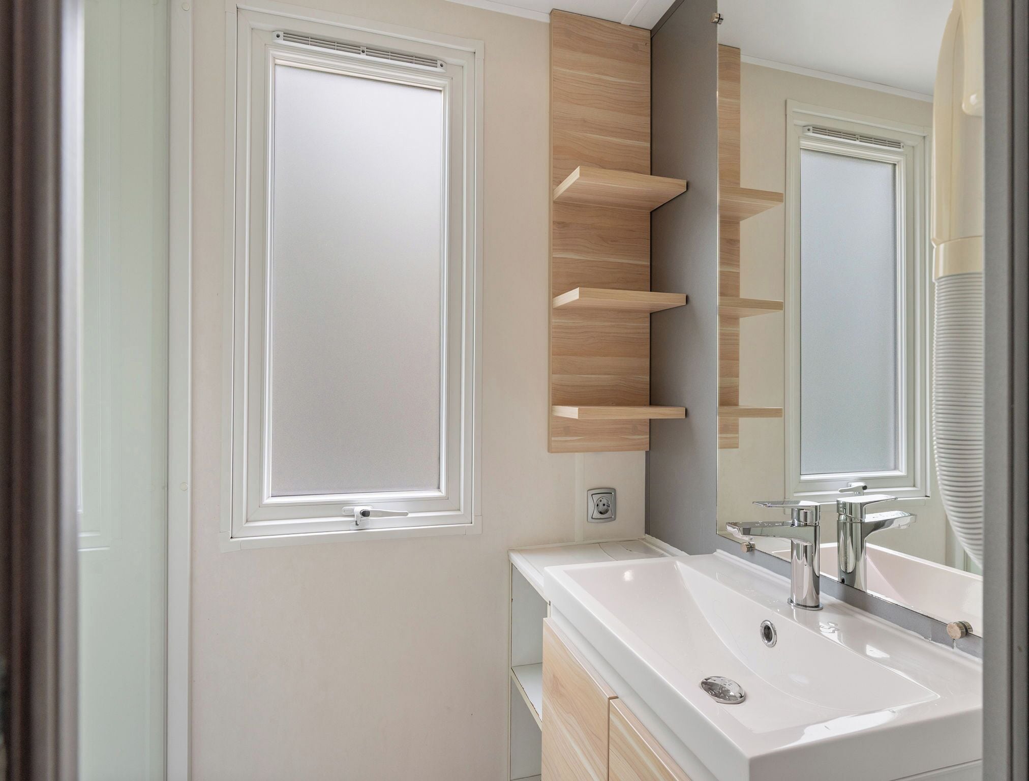 Een moderne badkamer met een grote spiegel, een witte wasbak en houten planken.