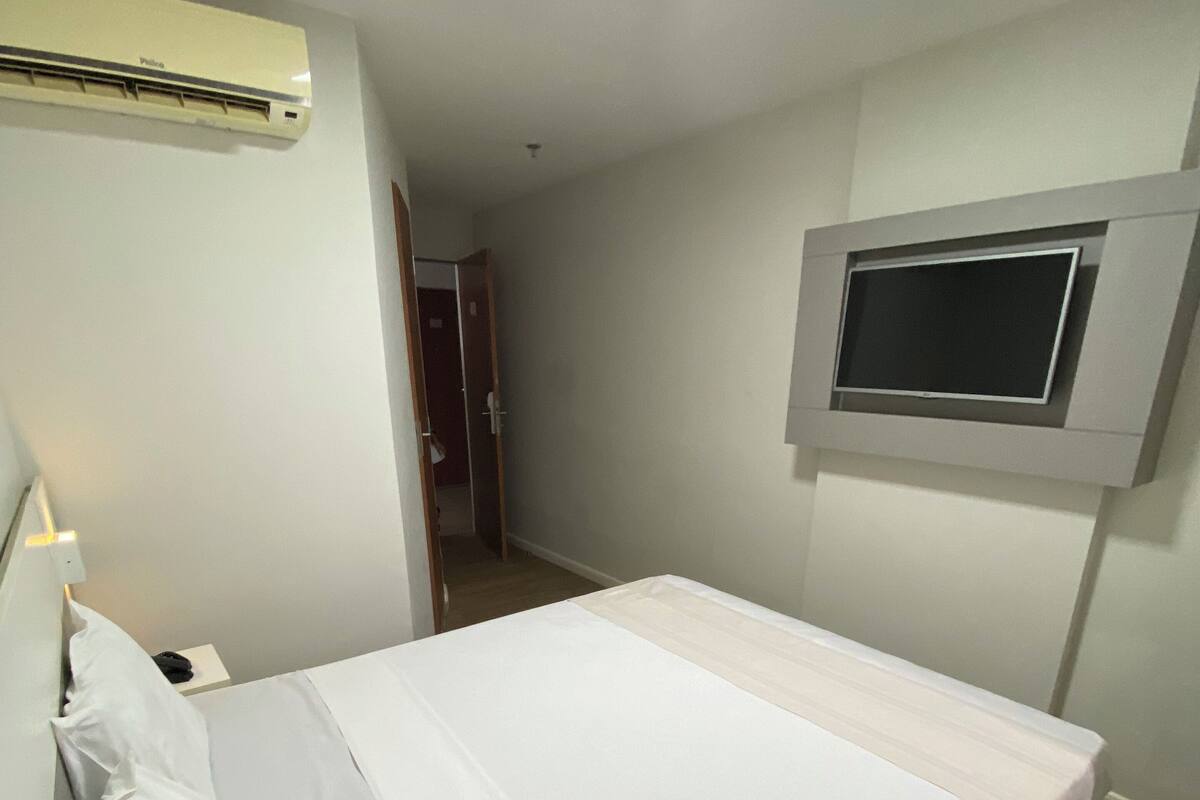 A bedroom with a bed, a TV mounted on the wall, and an air conditioning unit on the wall.
