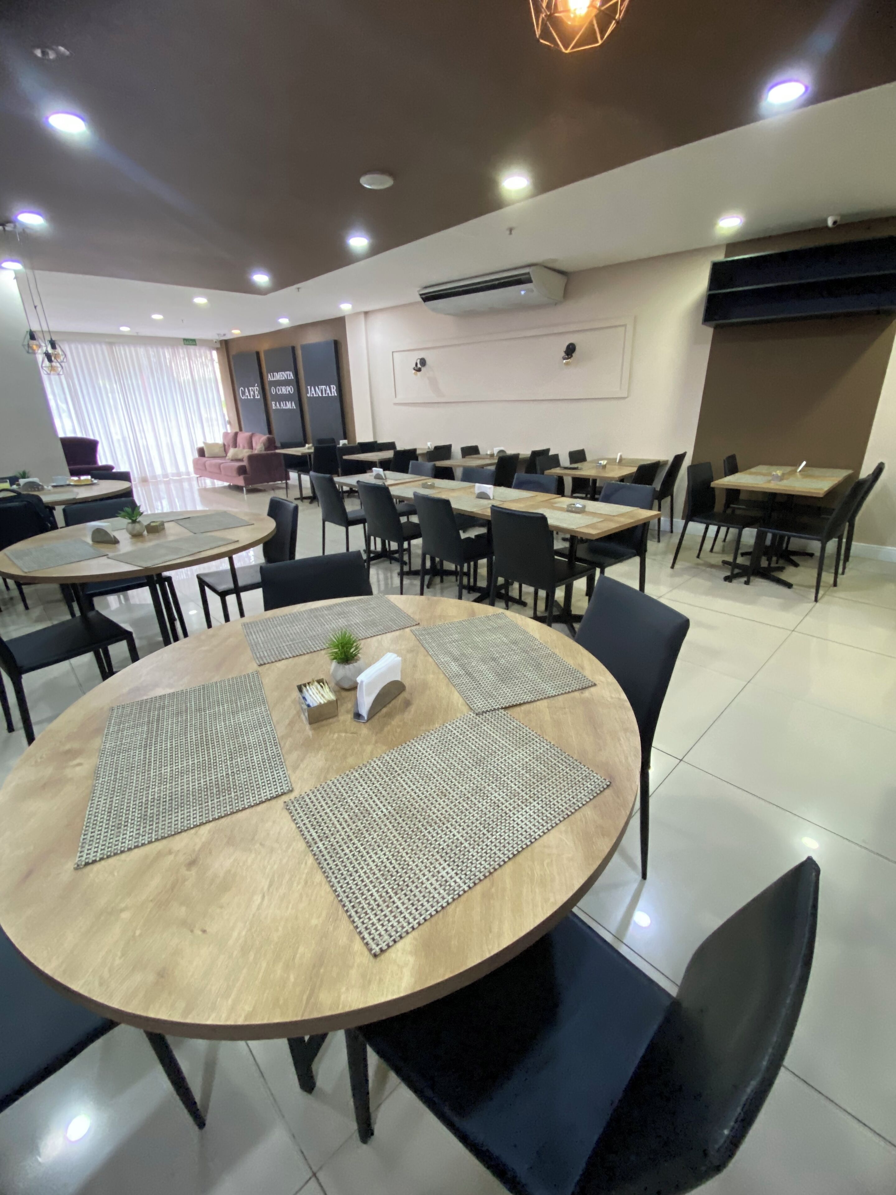 A modern dining area with round tables, black chairs, and a mix of natural and artificial lighting.