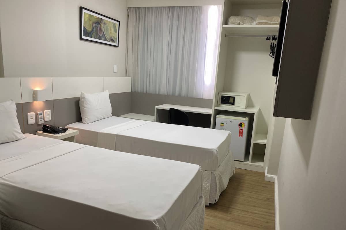 A hotel room with two beds, a desk, a microwave, and a closet.