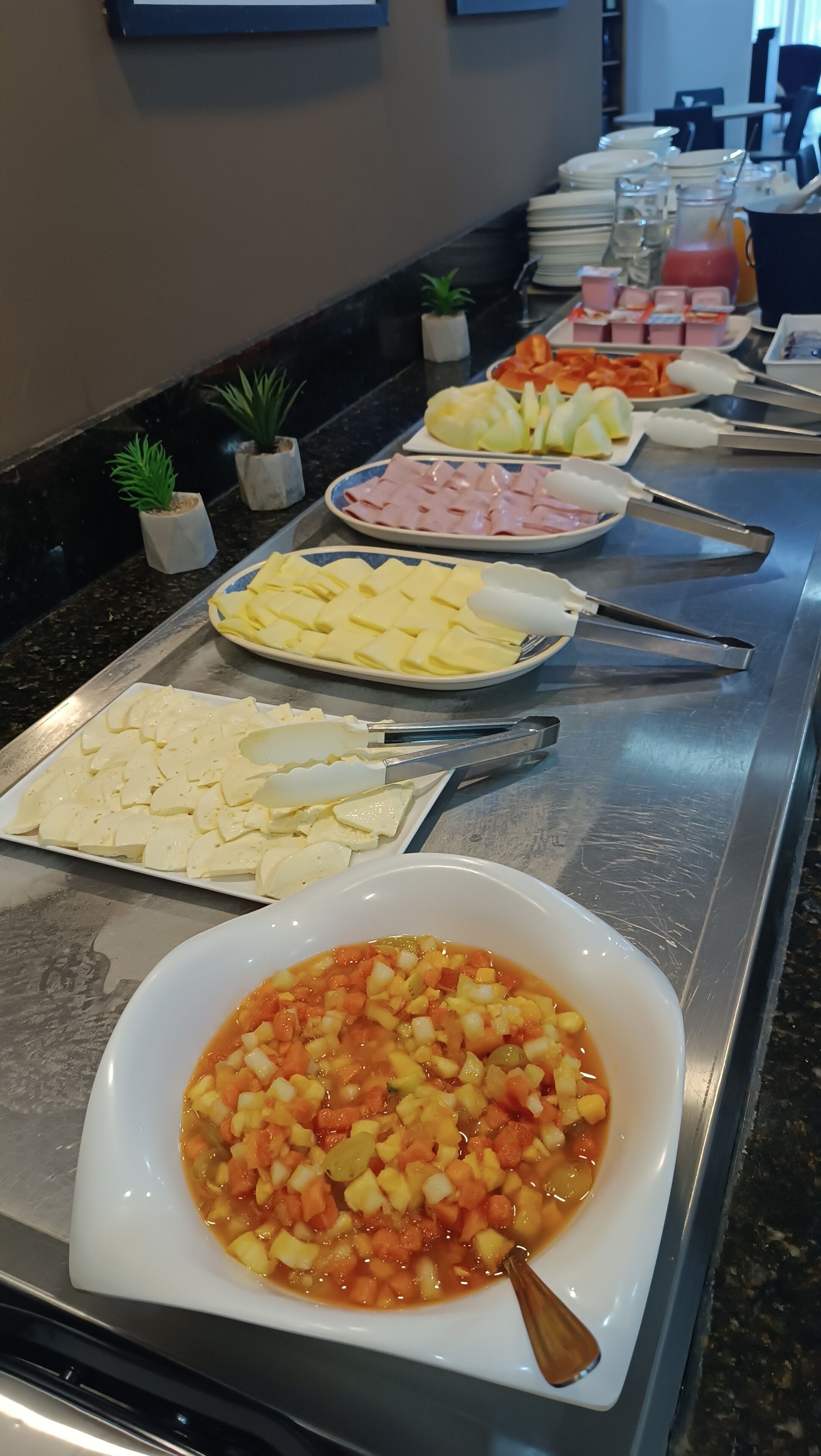 Un bufé con diversas opciones de comida, incluyendo queso, jamón y una ensalada de frutas.