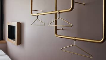 Une chambre moderne au design minimaliste, comprenant un lit, un téléviseur fixé au mur et un système de porte-manteaux en métal original.