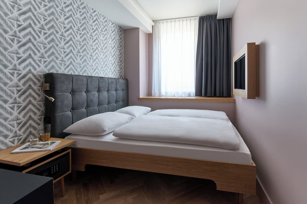 A neatly arranged bedroom with a bed, bedside table, and a window with curtains.