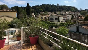 A terrace with potted plants, a railing, and a view of a hillside village with buildings and trees. - Beautiful Provencal villa of charm with beautiful views of village and castle (Villeneuve-Loubet)