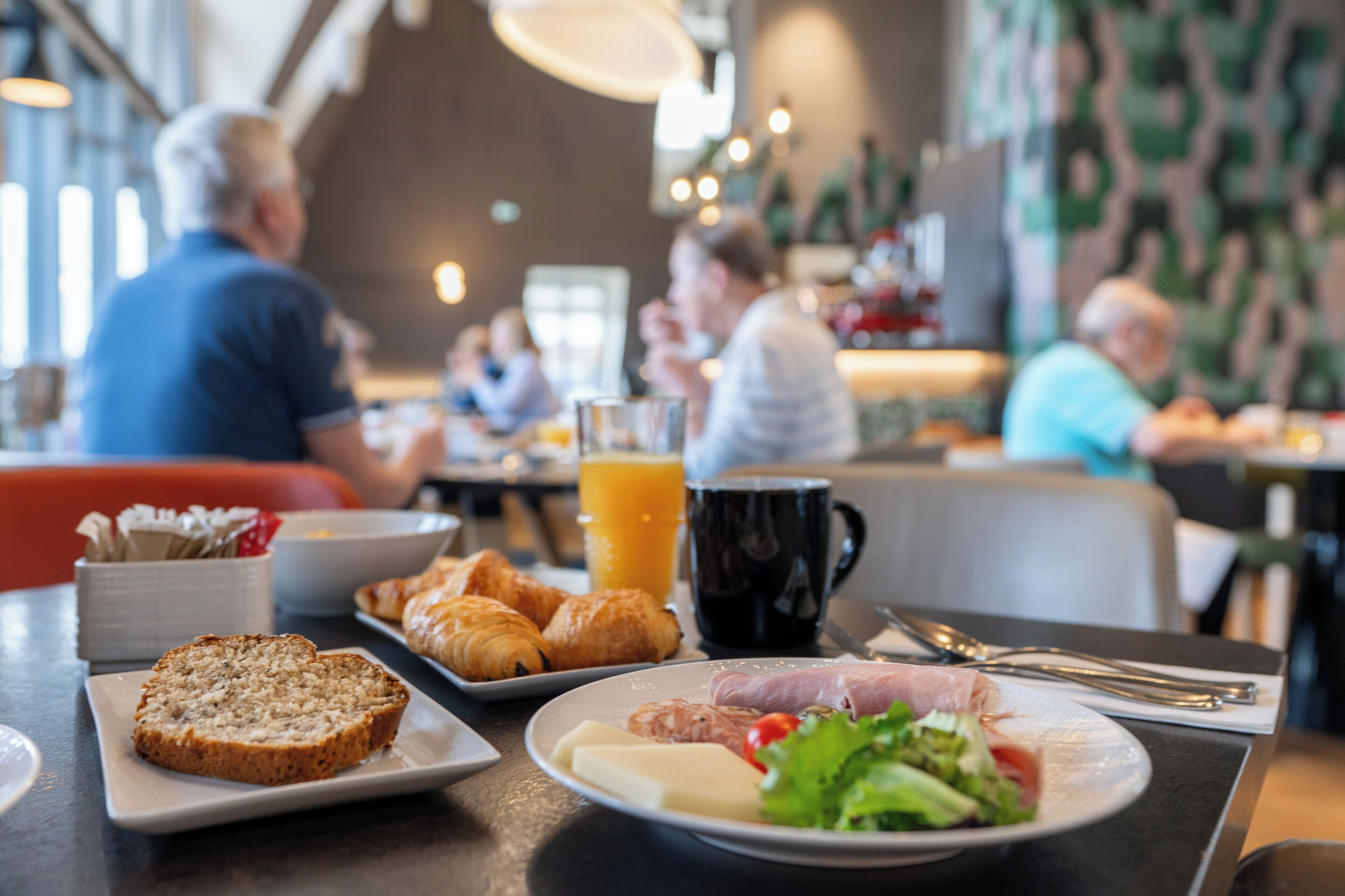 En matplats med bord som är dukade för frukost, med bland annat croissanter, bröd och en tallrik med ägg och grönsaker.