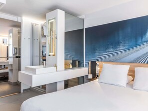 Moderni hotellihuone, jossa on suuri sänky, kylpyhuone, jossa on pesuallas ja peili, sekä suuri seinämaalaus.