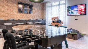 Une chambre moderne avec une table à plateau en verre, des sièges confortables, un grand ours en peluche et un téléviseur diffusant une scène festive.