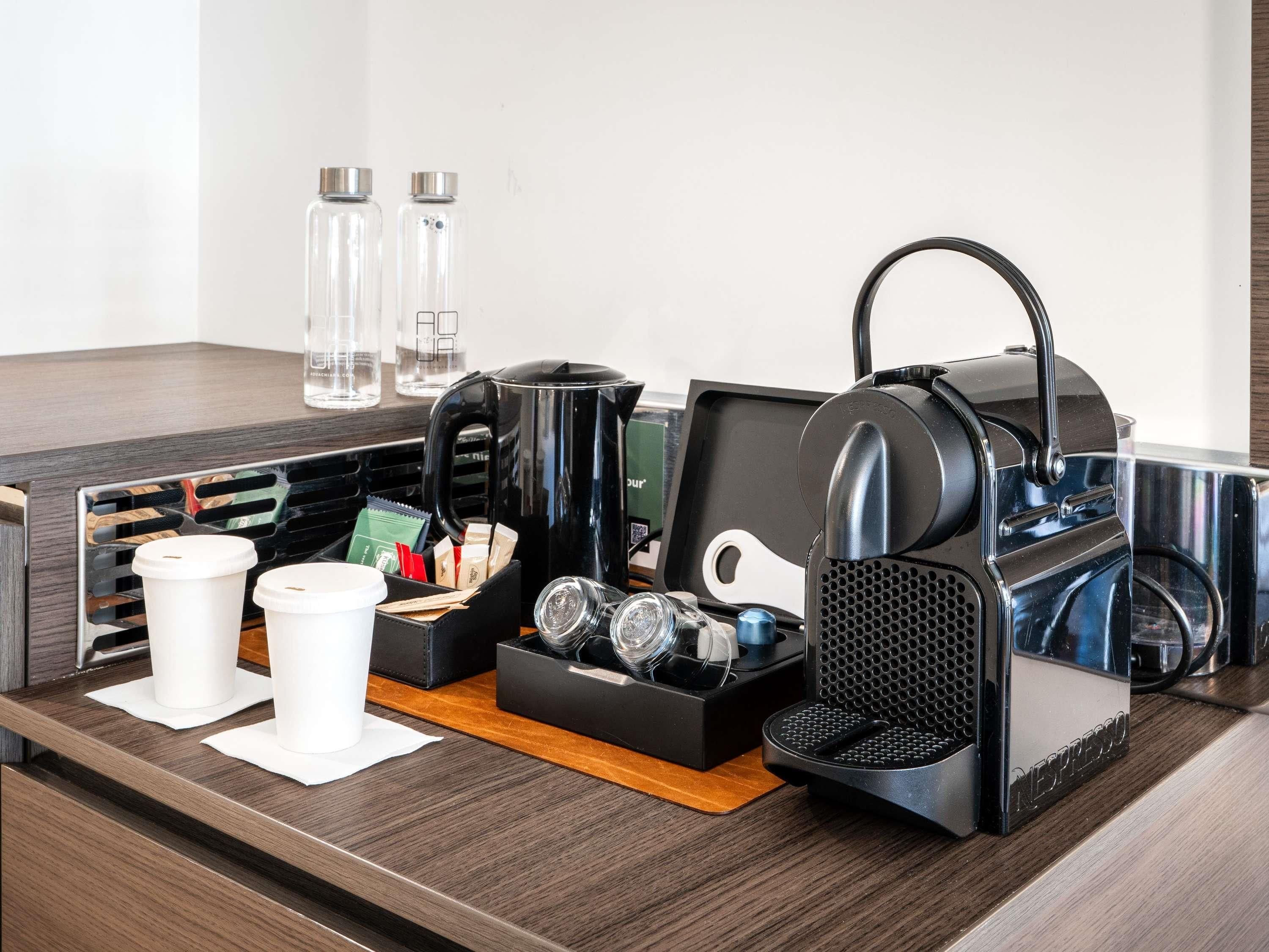 Un coin café équipé d’une machine à café, de tasses et d’un plateau contenant des dosettes de café et une cuillère.
