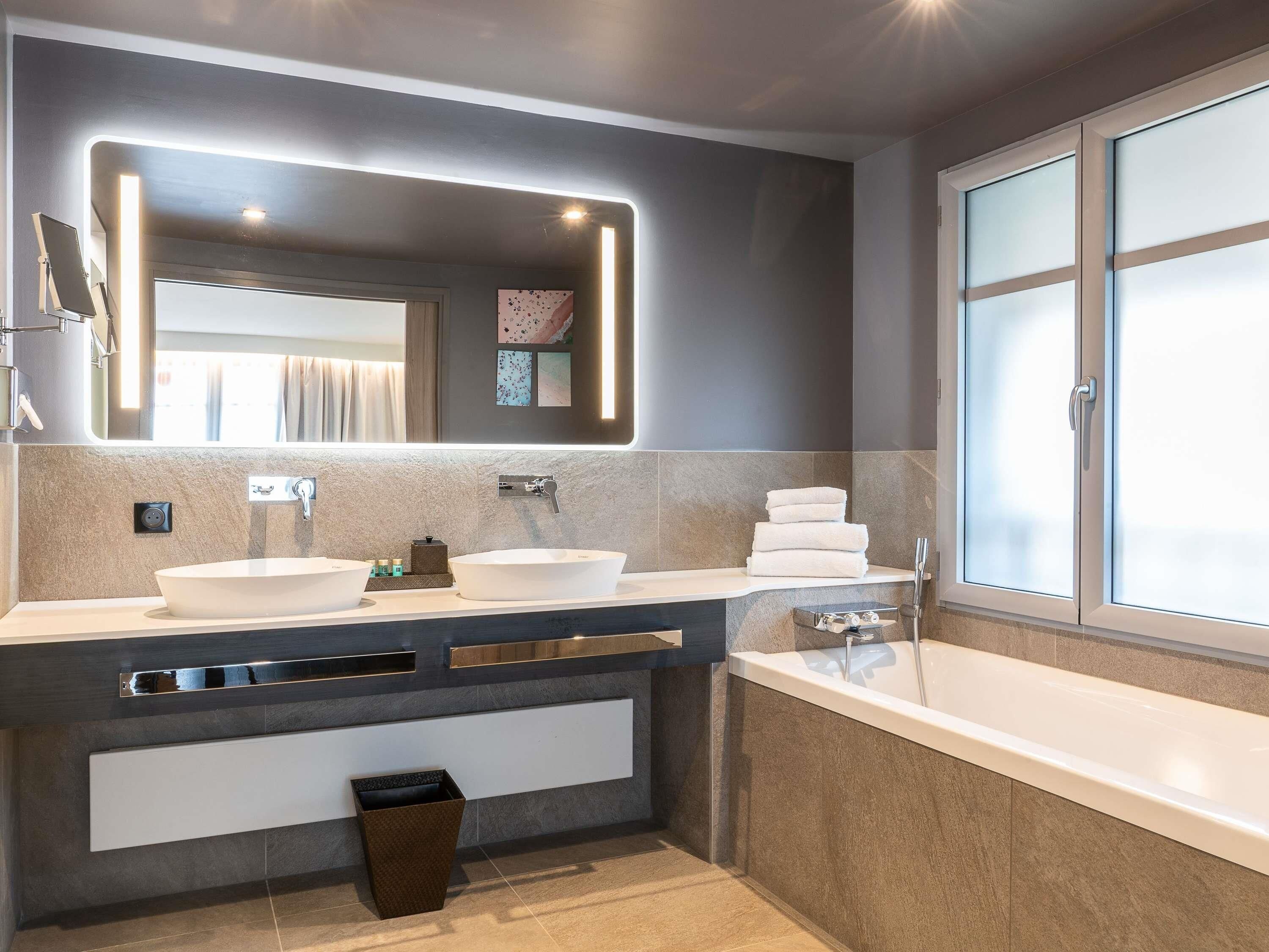 A modern bathroom with two sinks, a large mirror, and a bathtub.