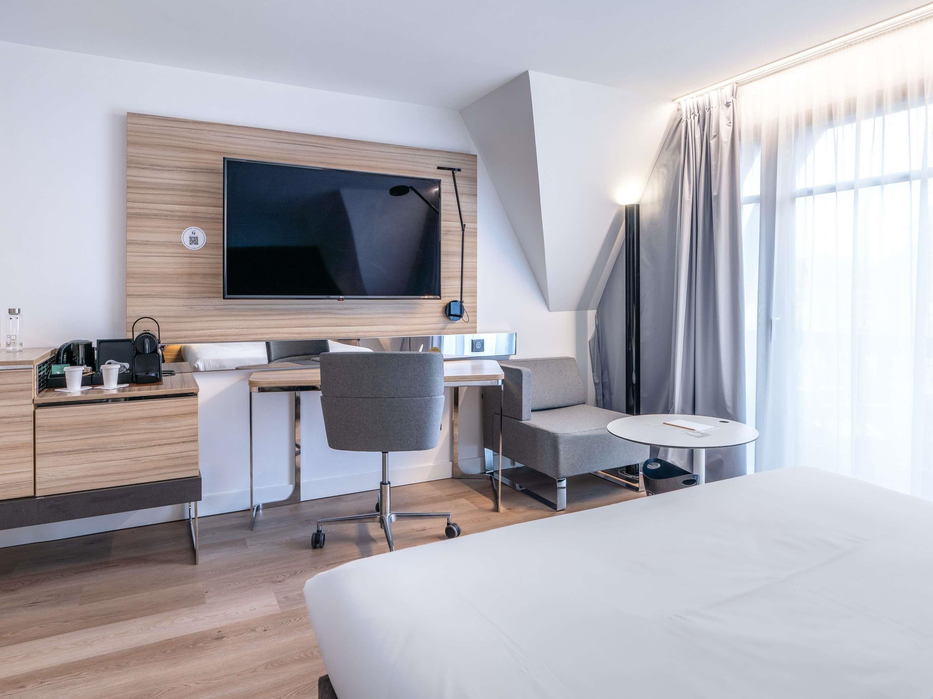 A modern hotel room with a large bed, a desk with a chair, a television, and a small table.