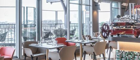 A modern restaurant with a high ceiling, large windows, and a central bar area.