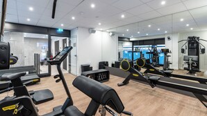 Une salle de sport moderne équipée de machines de cardio, d’appareils de musculation et dotée d’un mur entièrement recouvert de miroirs.
