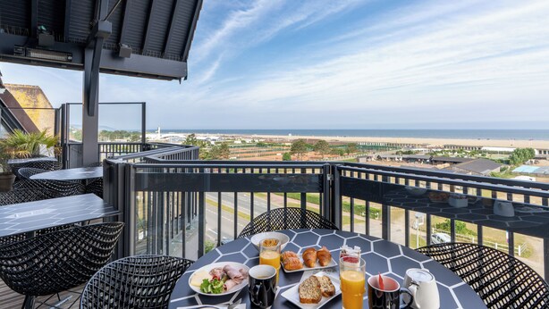 Un balcon avec une table préparée pour le petit-déjeuner, offrant une vue sur la plage et le paysage urbain.