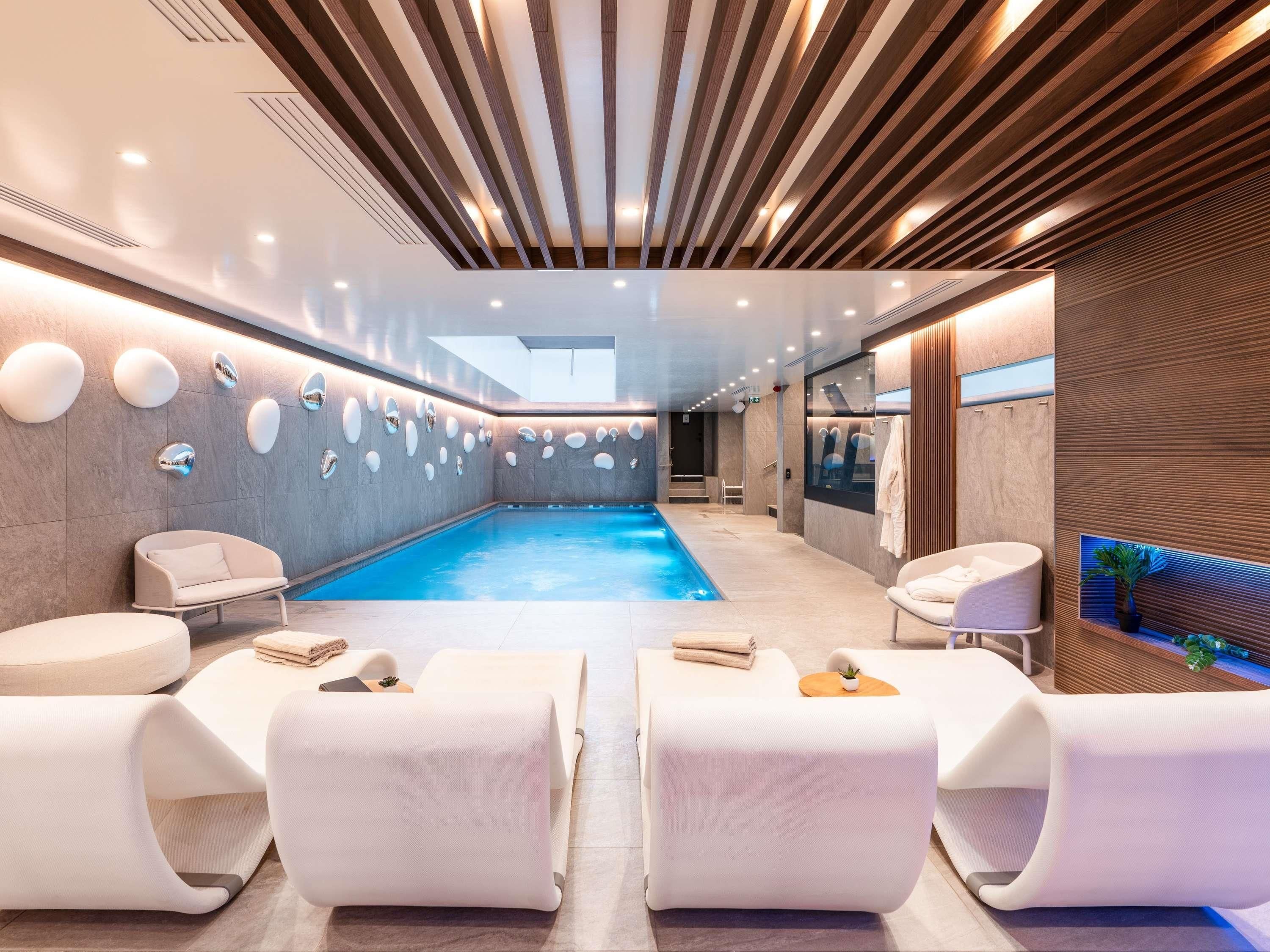 Un área interior de piscina moderna con vista despejada, asientos y una pared de madera con una planta.