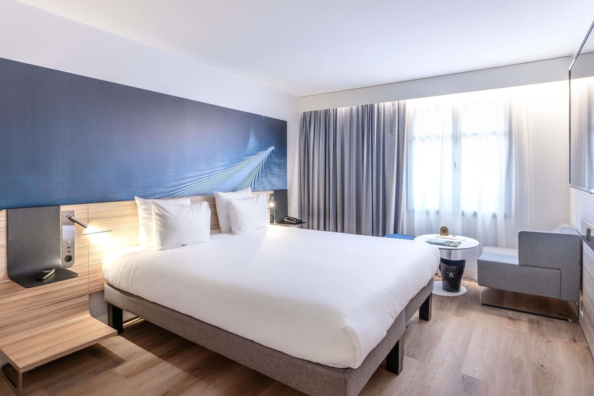 A modern hotel room with a large bed, bedside tables, a desk, and a chair.