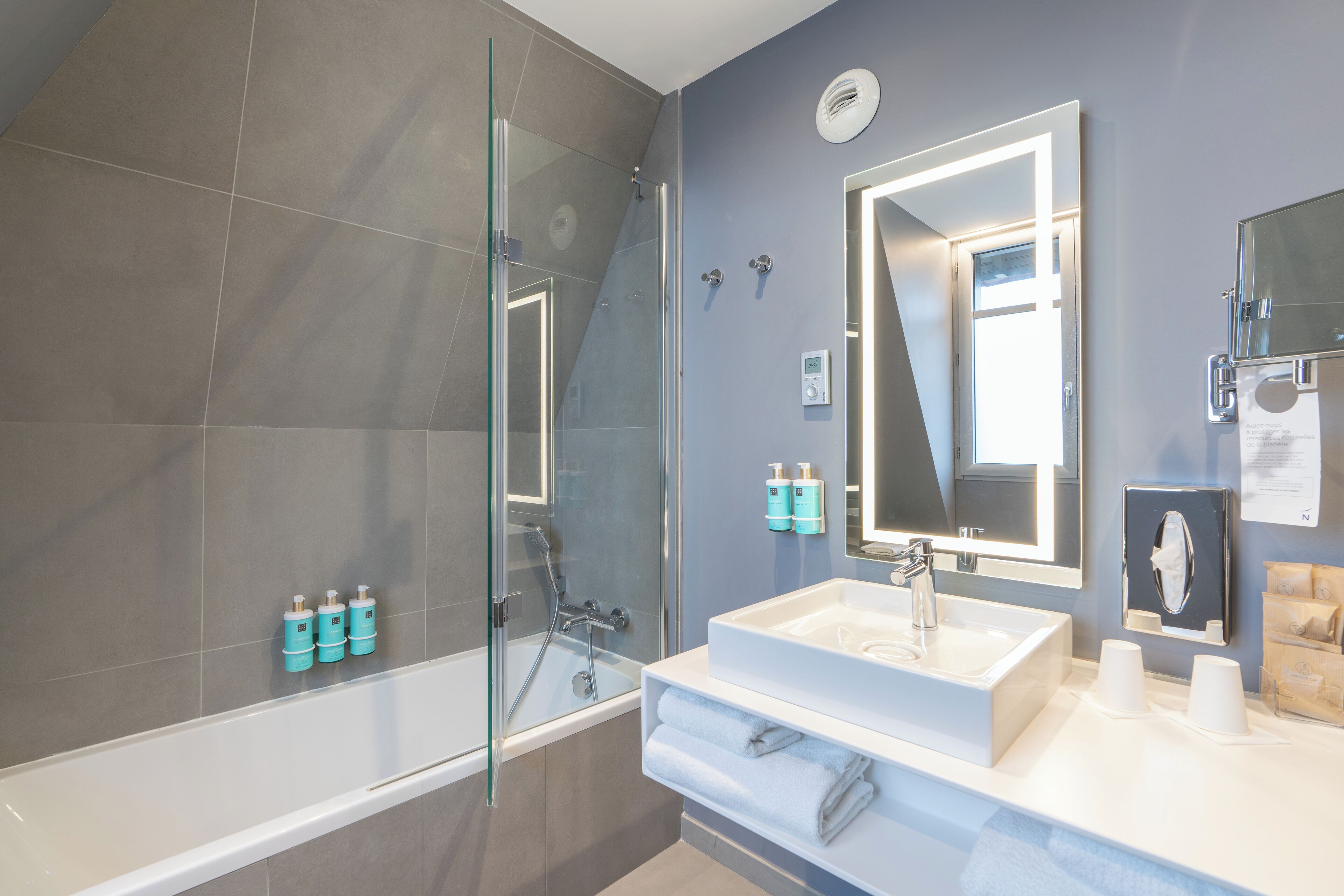 A modern bathroom with a glass shower enclosure, a white sink, and a large mirror.