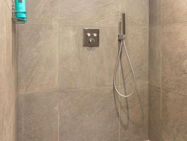 A shower with a handheld showerhead and a control panel.