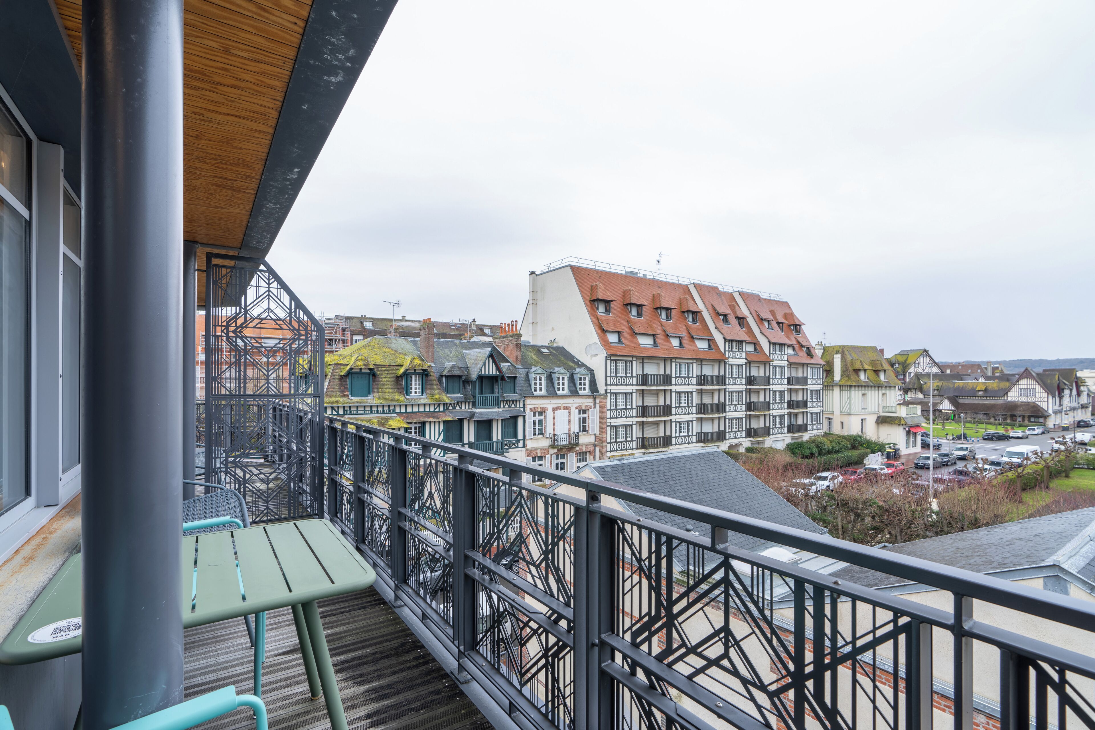 A balcony with a view of traditional European buildings, a wooden deck, and a metal railing.