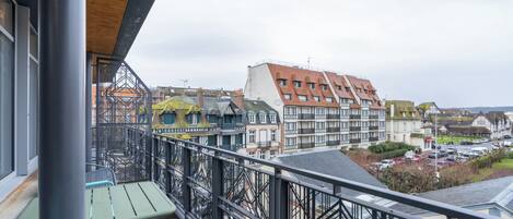 A balcony with a view of traditional European buildings, a wooden deck, and a metal railing.