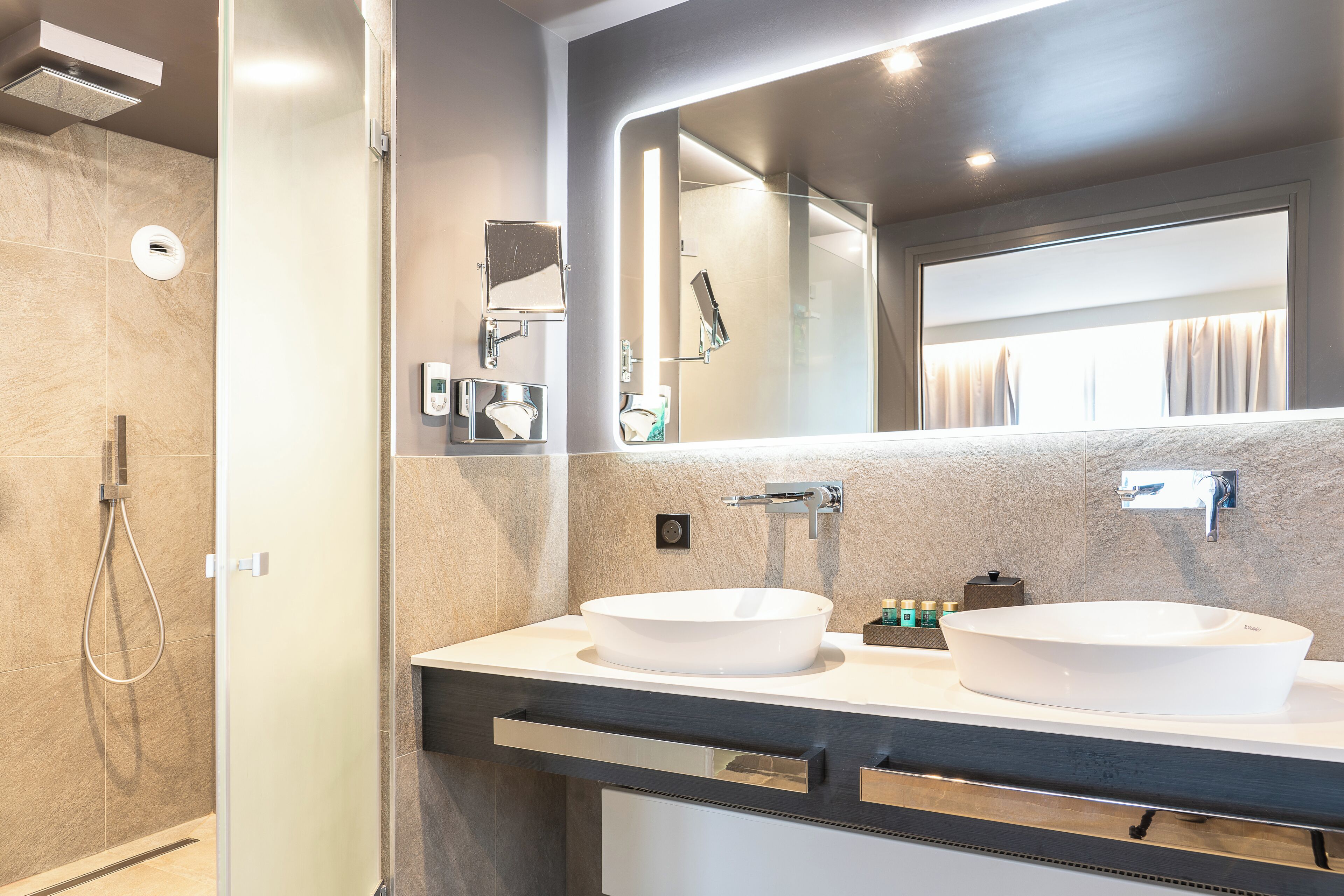 Une salle de bain moderne avec deux lavabos, un grand miroir et une douche.