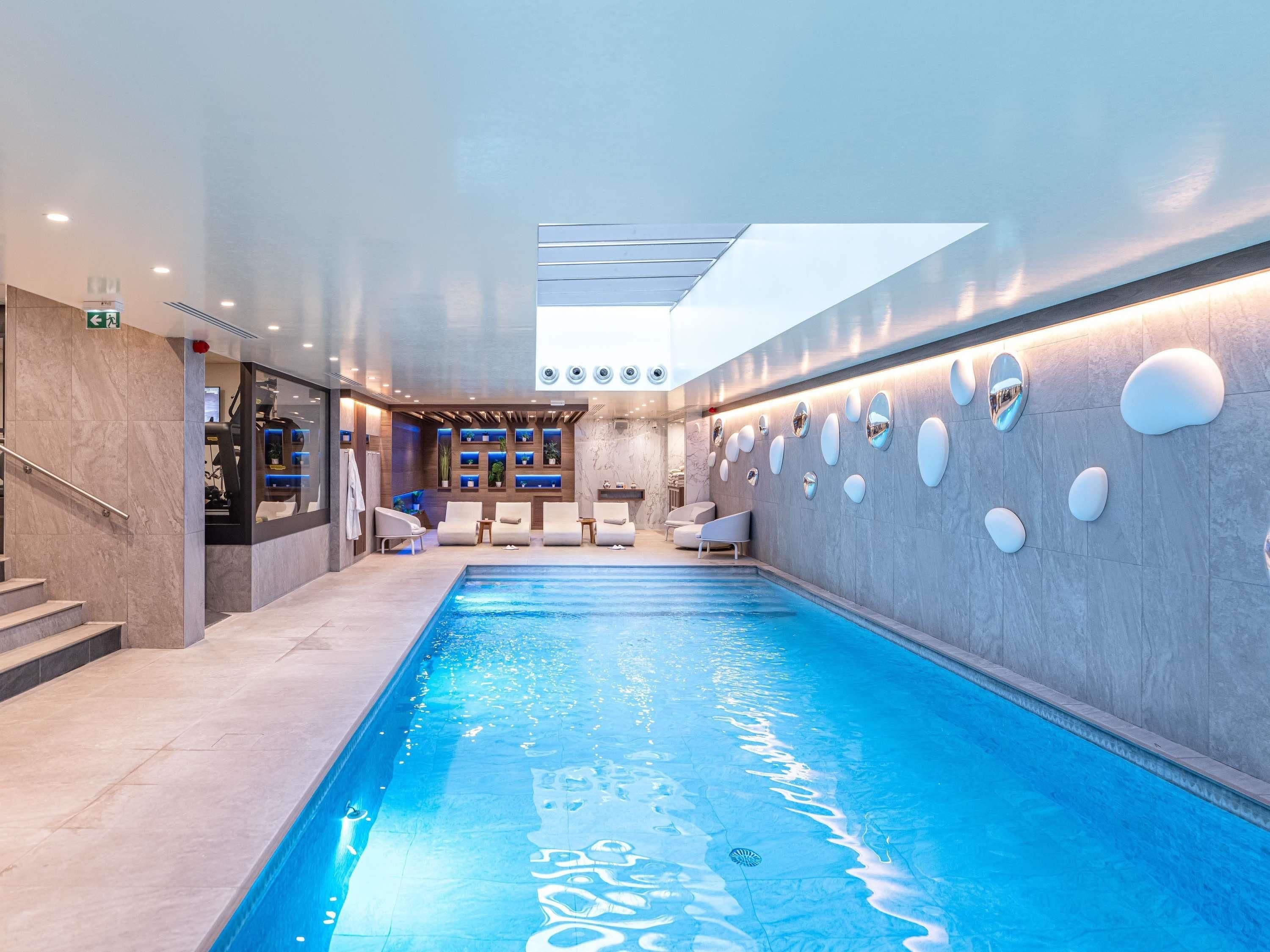 Piscina interna com vista clara do teto, área de estar com cadeiras e um balcão de recepção.