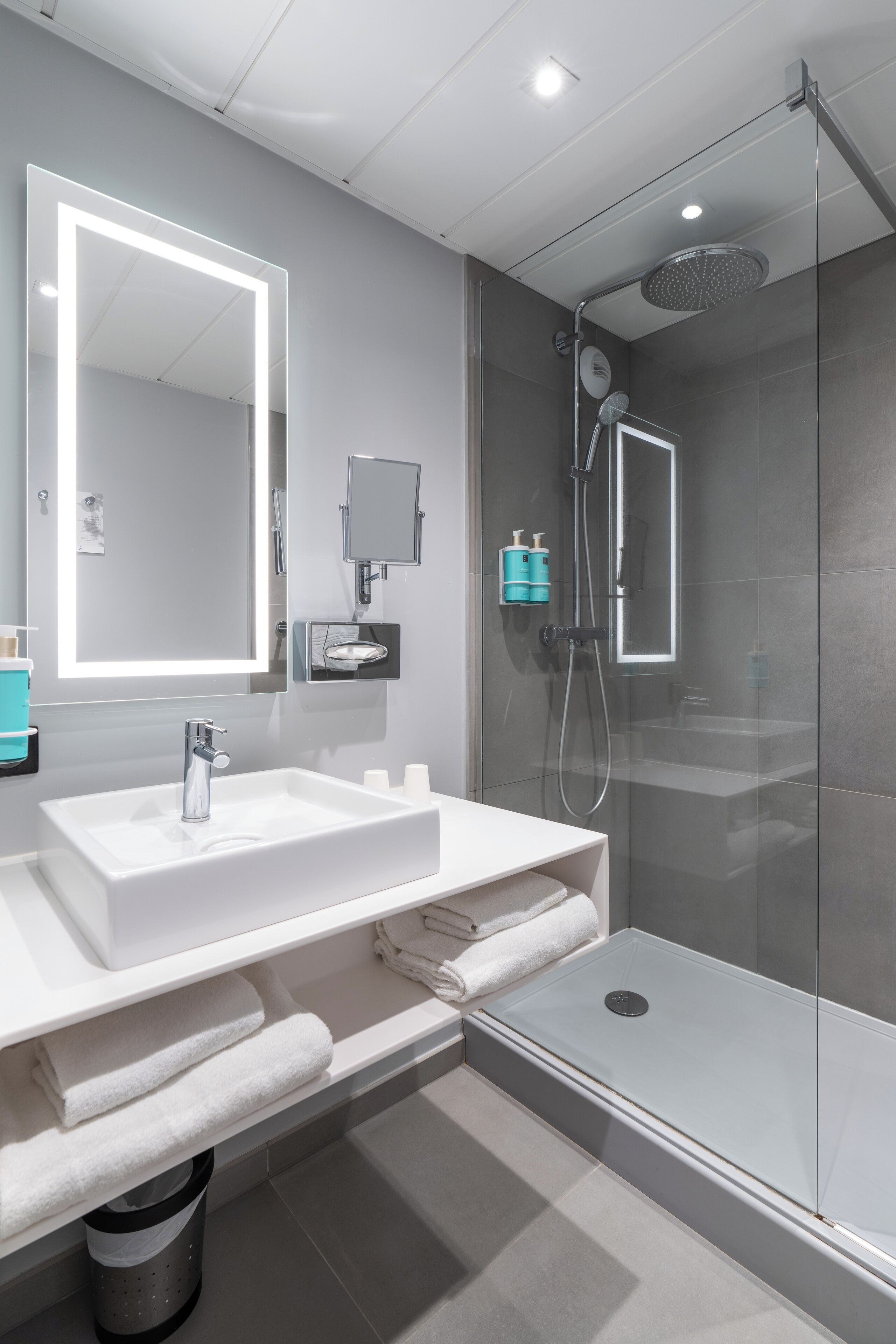 A modern bathroom with a white sink, a large mirror, a glass-enclosed shower, and a towel rack.