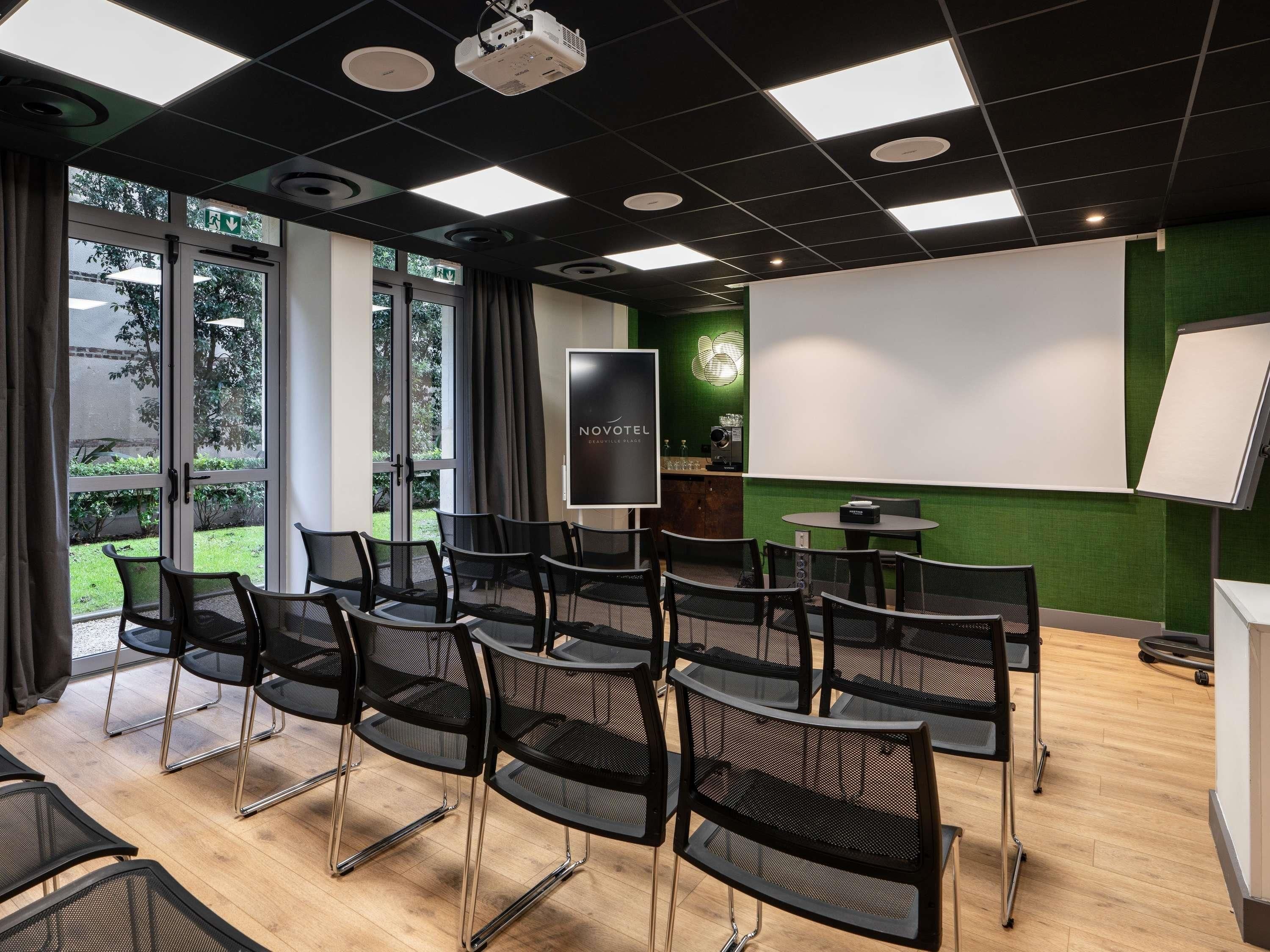 Une salle de conférence équipée d’un projecteur, d’un écran et d’un mur vert.